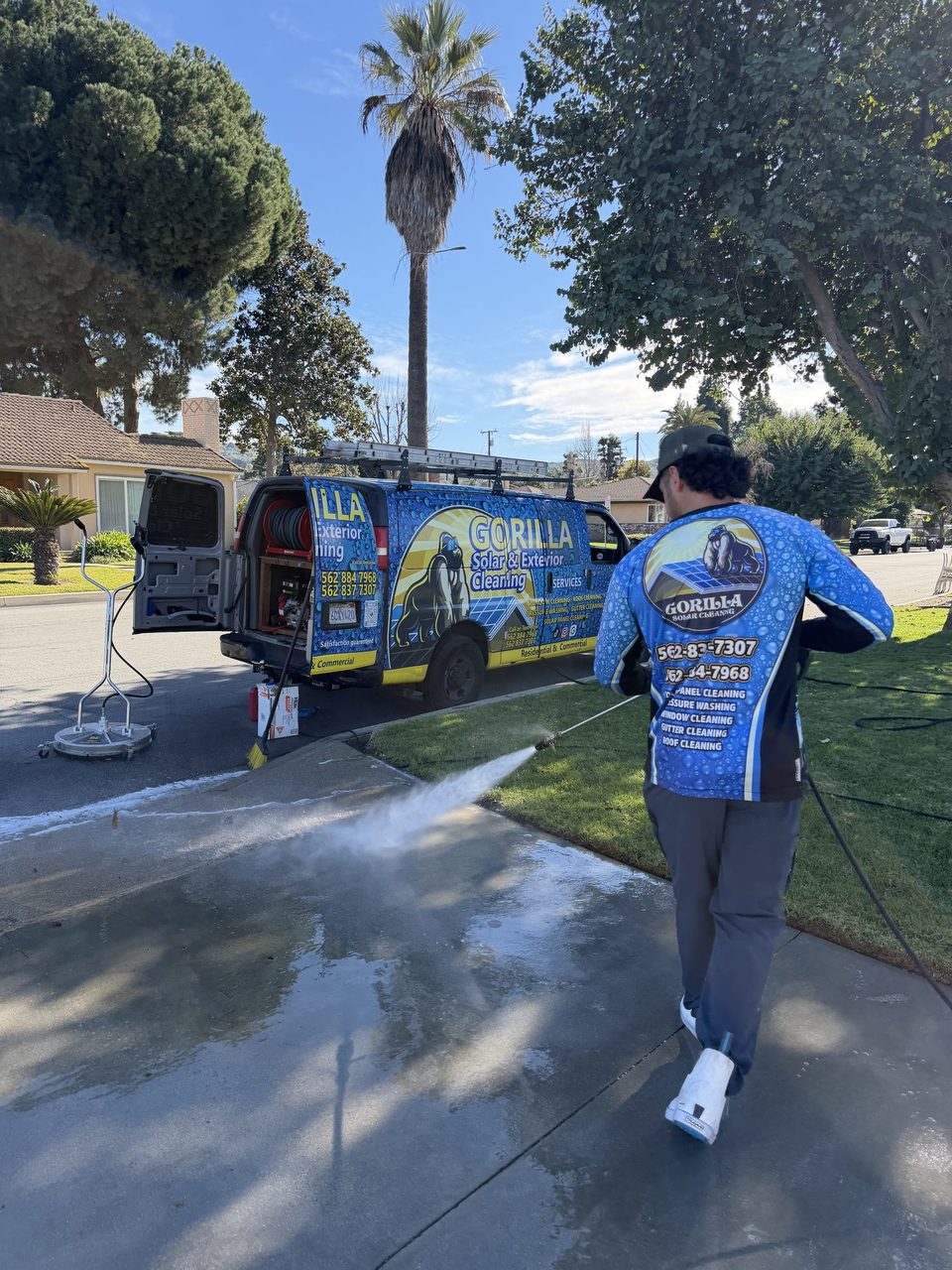 Gorilla technician pressure washing a concrete driveway next to the branded van in Los Angeles