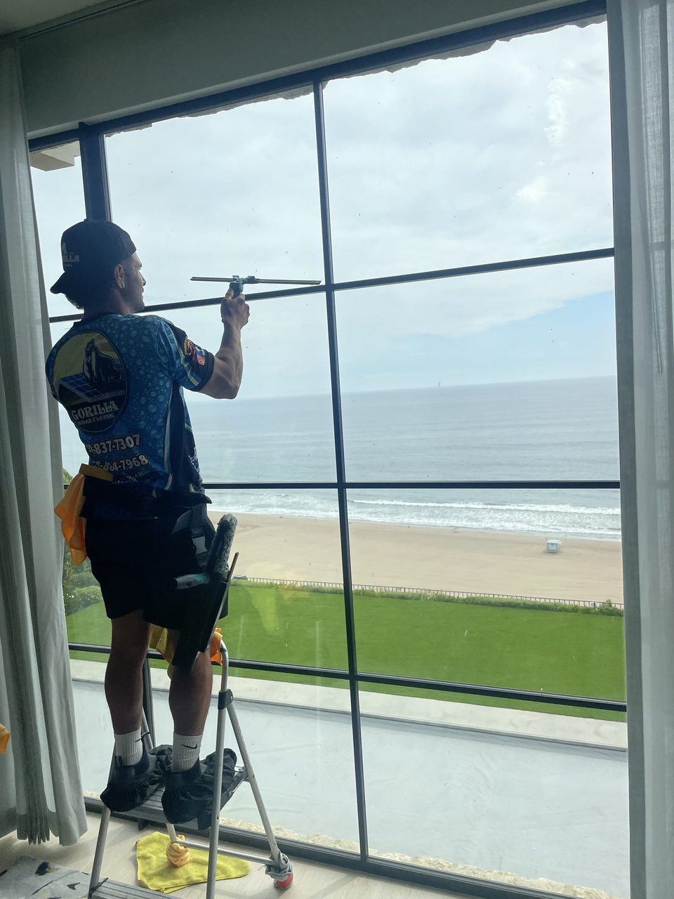Gorilla technician squeegee-cleaning a large beachfront window in Los Angeles
